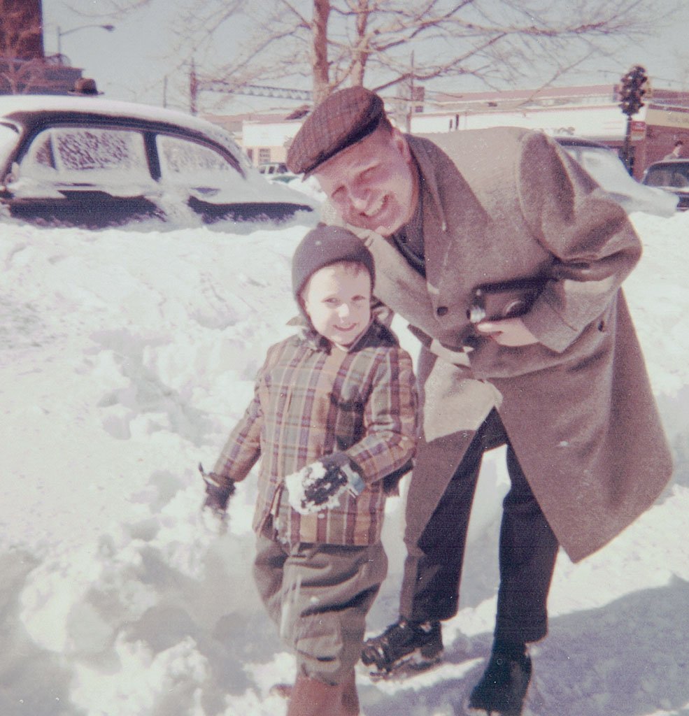 My father, holding his movie camera and wearing a brown coat and cap, bends towards me as I stand, bundled up for winter, in front of a mound of snow taller than I was at four years old. The piles of snow created by the shoveling of the sidewalk reach to the base of the window of a parked car.