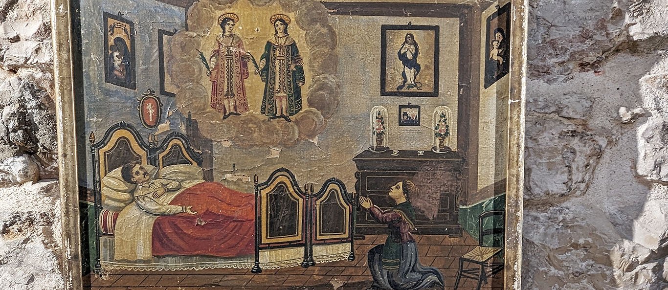 A painting shows a man lying in a large double bed. A woman kneels in the room and sees a vision of two haloed martyrs holding palms. The room has several framed images of the Virgin Mary on the walls.