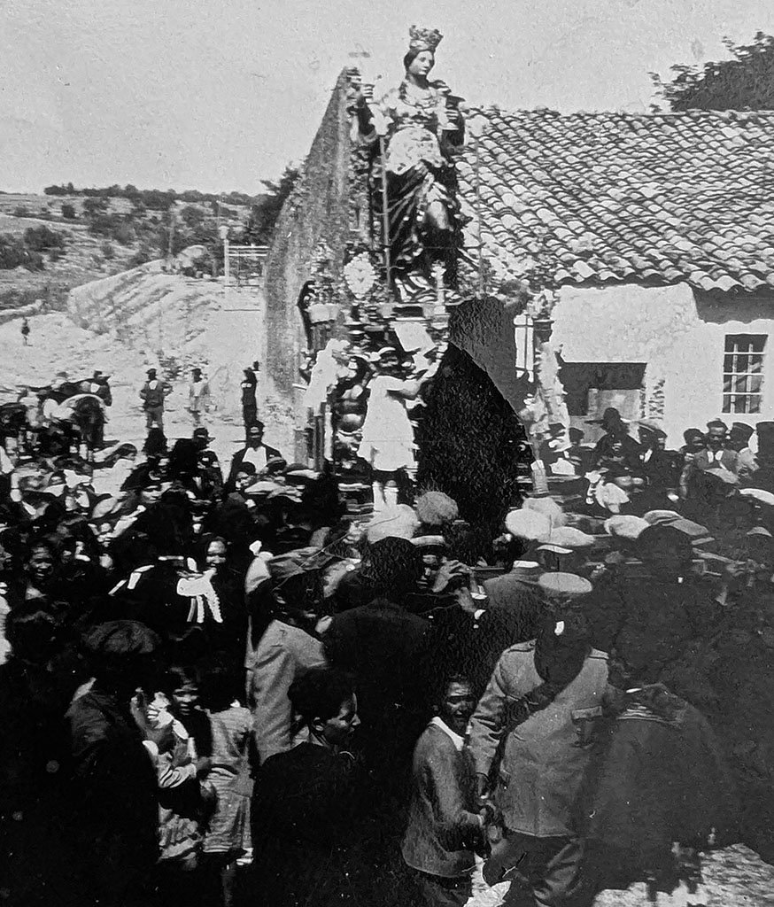 The photograph looks over the heads of a crowd of people with some children in the foreground. At the center, a crowned statue of Santa Sofia is raised on a large, decorated platform or float. My mother (at six years old) stands on the raised platform looking towards the camera.