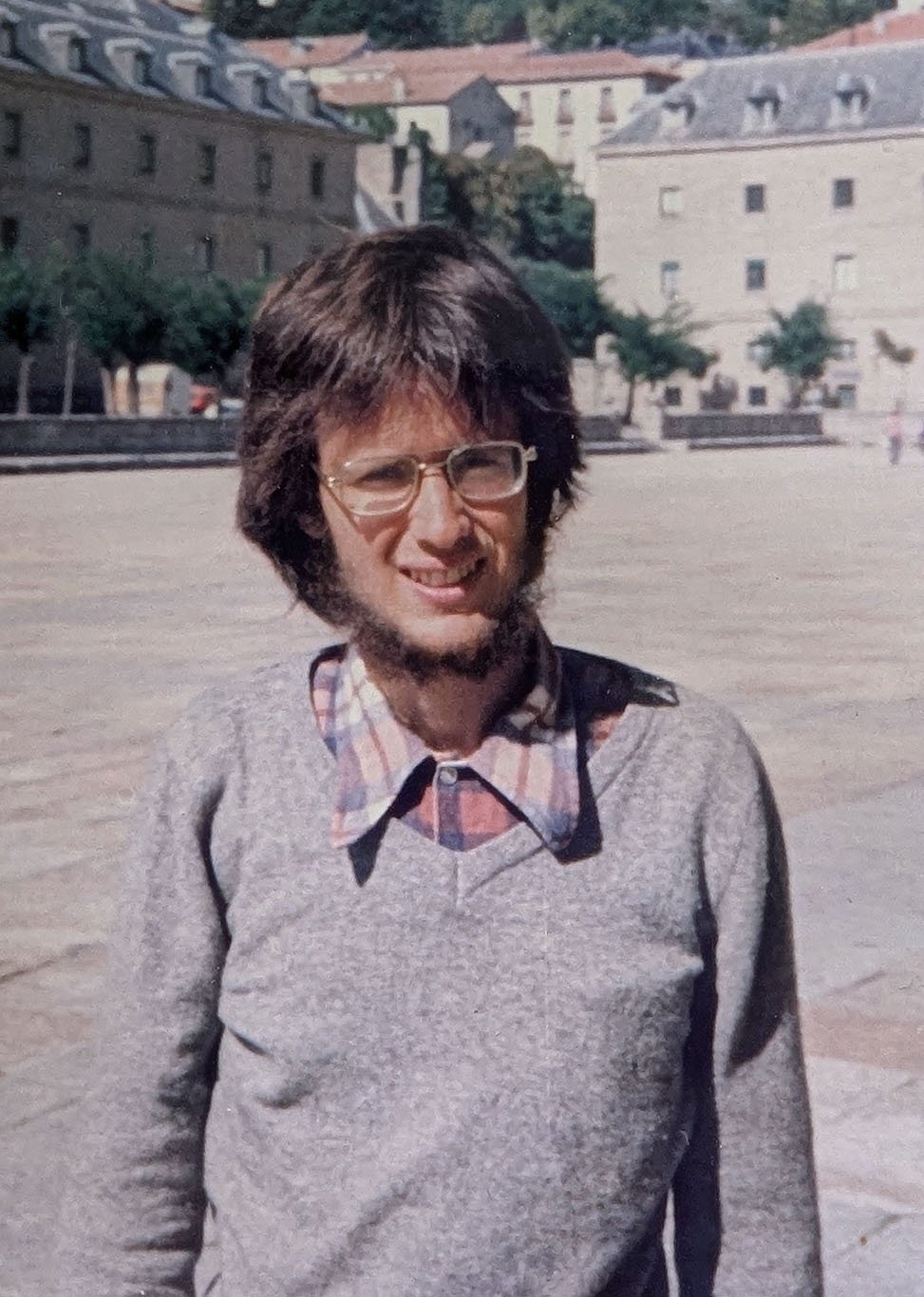 With long hair parted in the center, a thin beard as a rim around my face, a light grey sweater, and the faded collar of an old flannel shirt, I am very thin at the end of my Watson fellowship, standing in the square of El Escorial in October 1978.