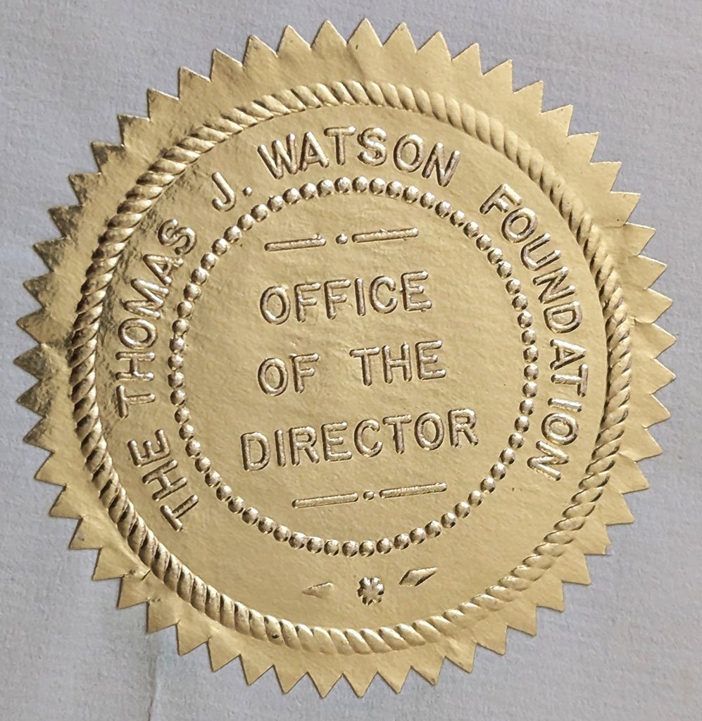 A round gold seal with a toothed border. Inside it says, 'The Thomas J. Watson Foundation' and 'Office of the Director'.