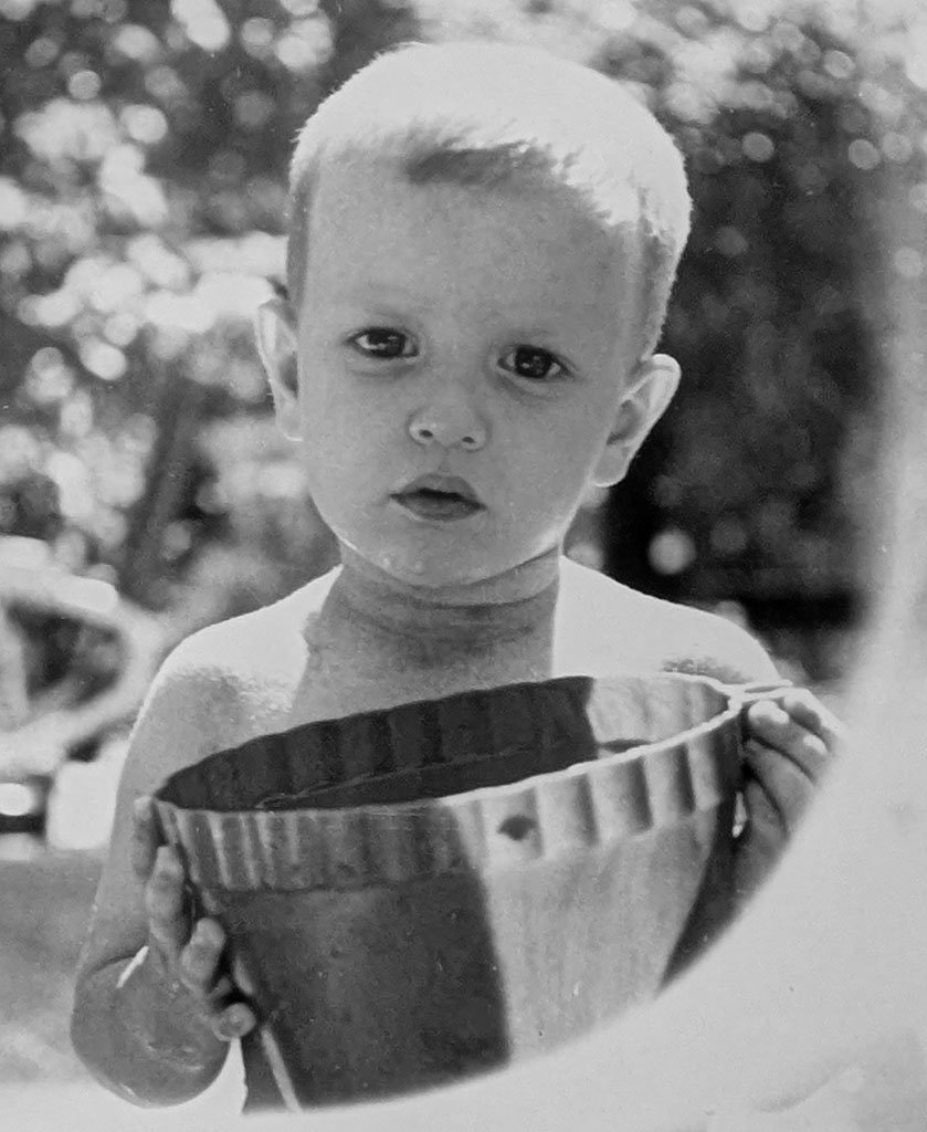 Photograph of me at almost 3 years old. I have a serious expression and I'm holding a pail.