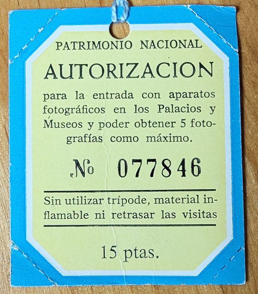 This is the tag that the Patrimonio Nacional sold in 1978 for 15 pesetas. It reads 'Autorización para la entrada con aparatos fotográficos en los Palacios y Museos y poder obtener 5 fotografías como máximo. Sin utilzar tripode, material inflamable ni retrasar las visitas.' It allowed a maximum of five photos without a tripod.