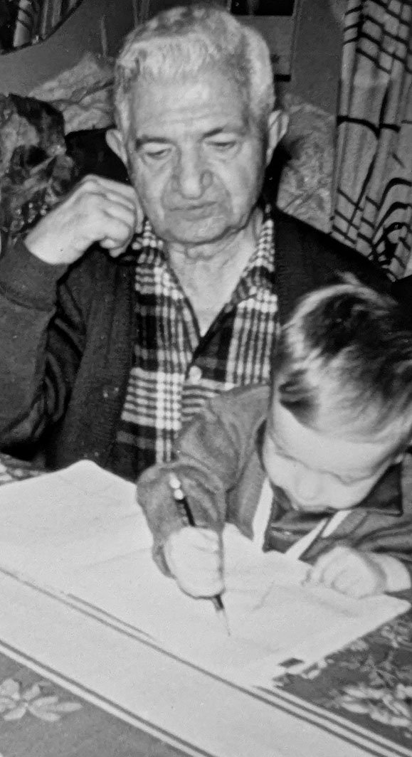 My grandfather looks on while I write or draw with a pencil on a piece of paper or notebook. My head full of hair is bent over the page and I am clutching the pencil with a fist.